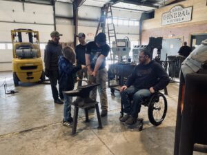 Man in wheelchair and boys work on a blacksmithing project together at Kilroy's 
